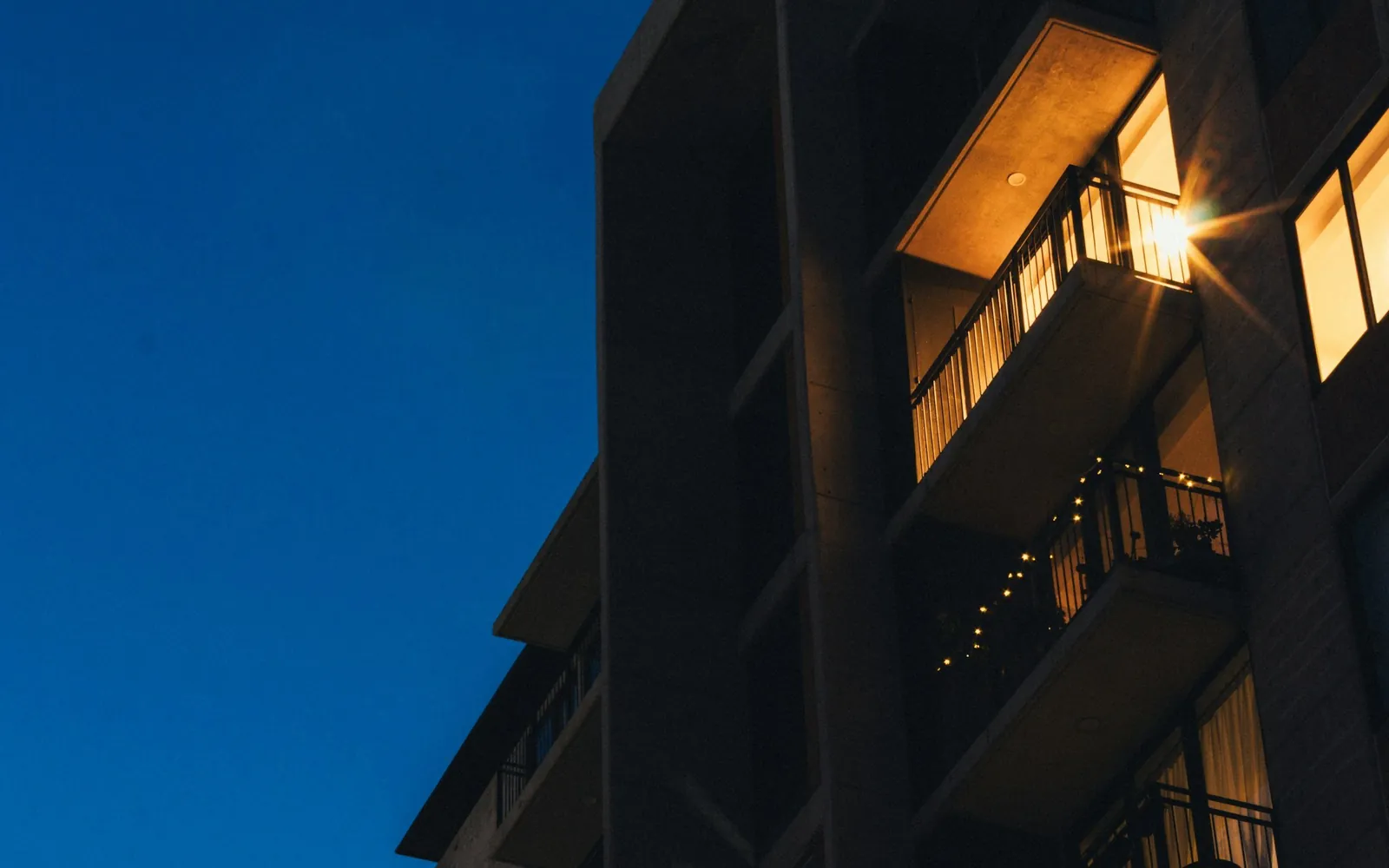 A modern apartment building at dusk with warm light on the balconies